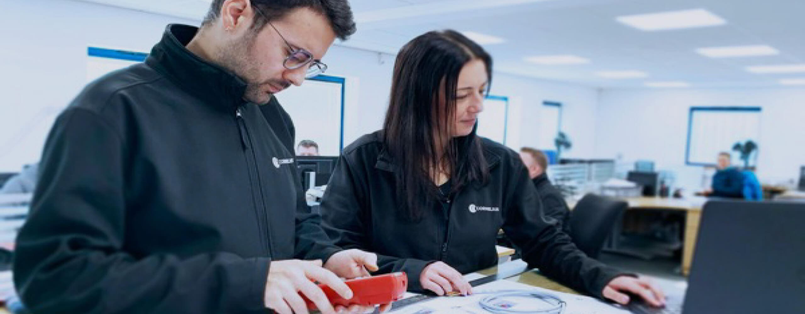 A woman and man looking at electronics wiring in a factory setting